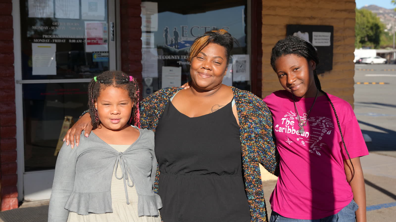 A mother and her two daughters standing together outside the entrance of the East County Transitional Living Center in El Cajon