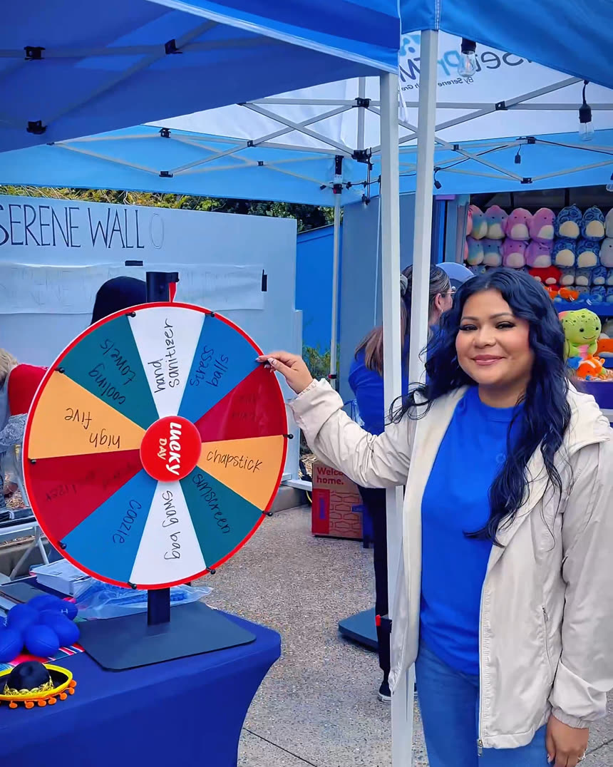 A MindSet and Serene Health Group team member at their festival booth with a Lucky Day prize wheel during Taco Fest at SeaWorld
